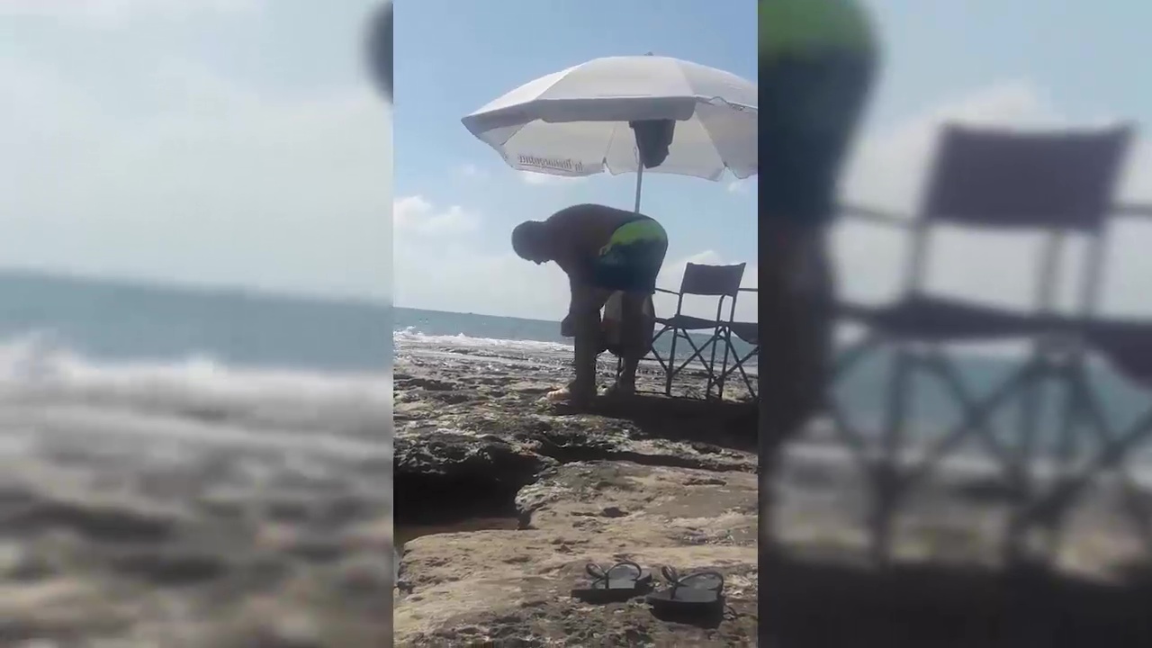 Imagen de Un hombre utiliza un taladro para clavar su sombrilla en las rocas de una cala